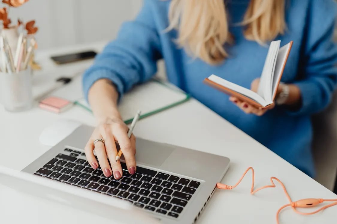 Person learning how to start a business blog, typing on a laptop with a notebook